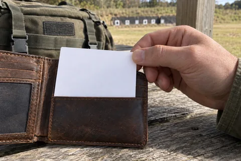A hand removing a small reference card from a brown leather wallet on a range bench